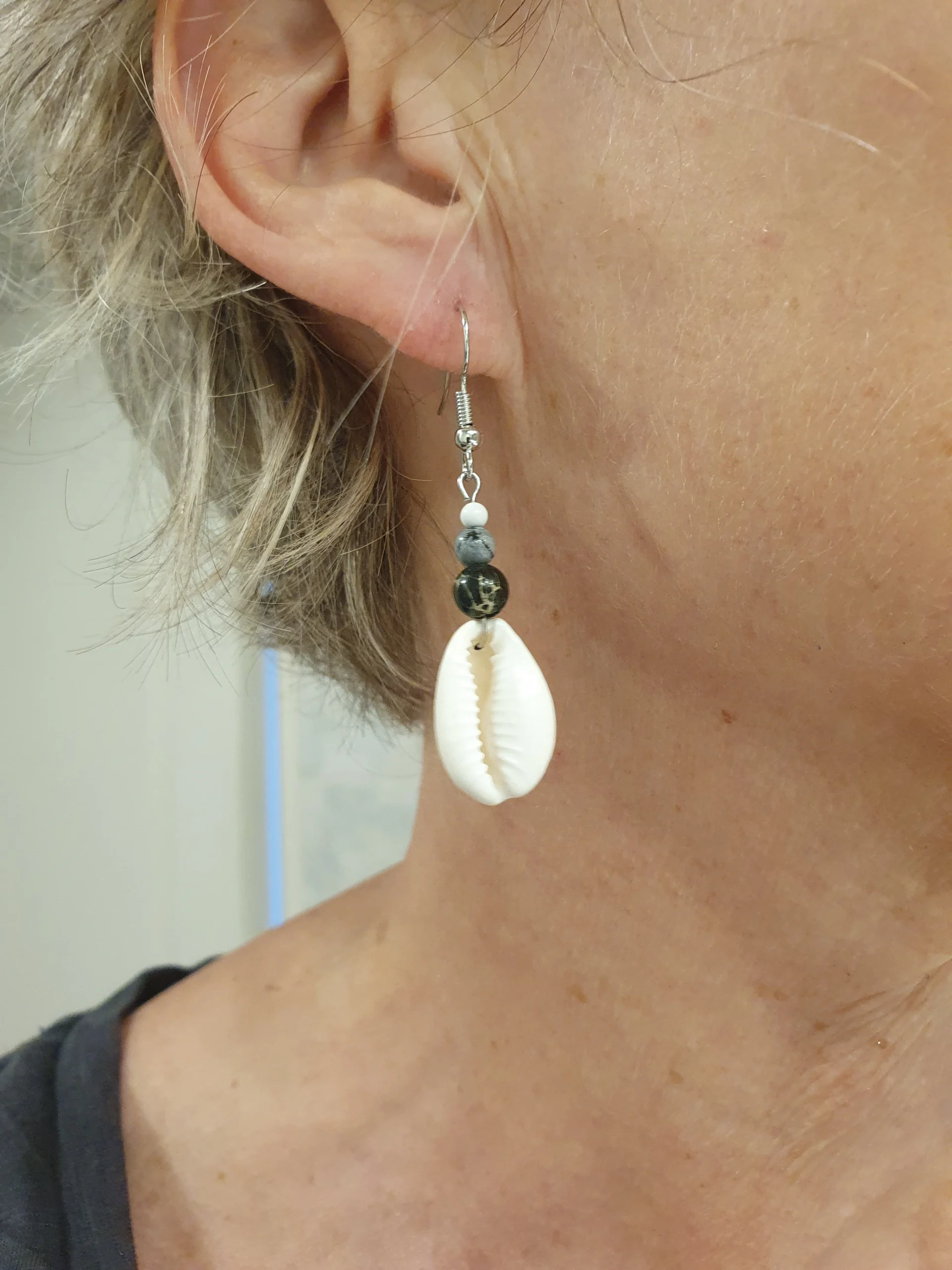 Boucles d'oreilles Kaura avec coquillage cauri, jaspe gris et crochet en acier inoxydable argenté. Vue portées.