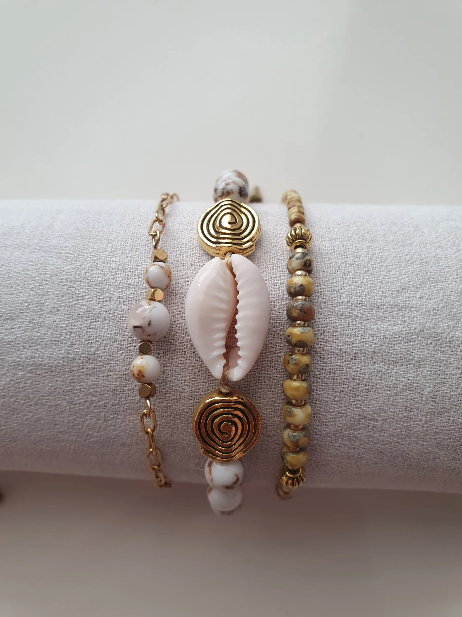 Bracelet Trio Ocealis avec coquillage cauri et perles de pierre naturelle. Modèle blanc. Vue sur coussin