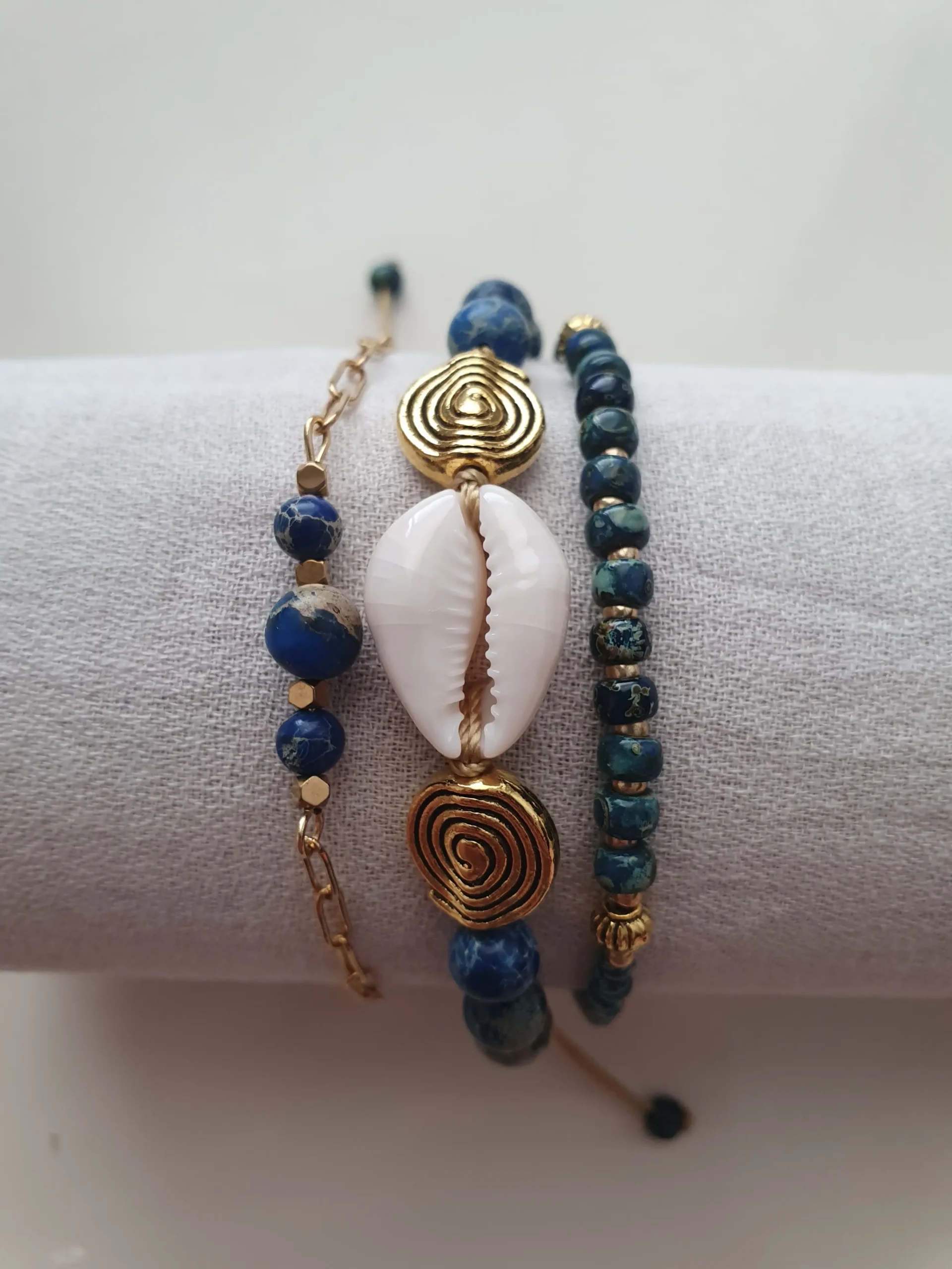 Bracelet Trio Ocealis avec coquillage cauri et perles de pierre naturelle. Modèle bleu. Vue sur coussin