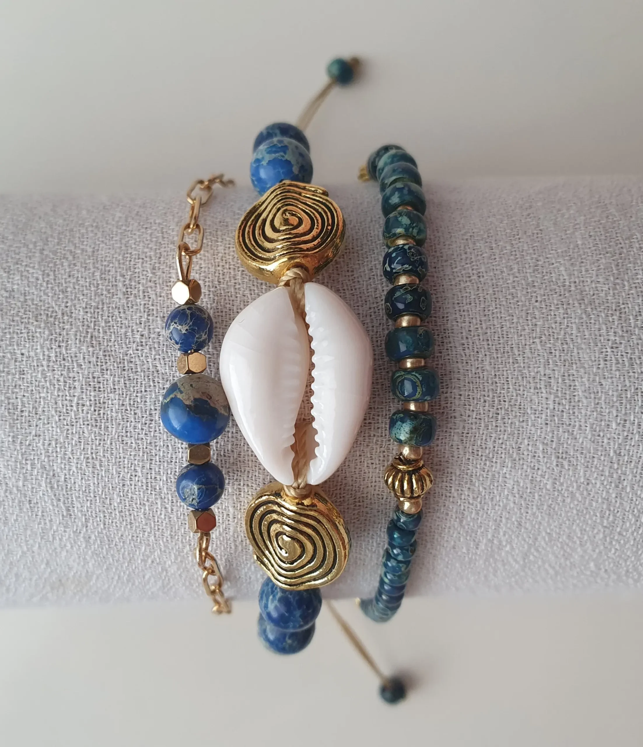 Bracelet Trio Ocealis avec coquillage cauri et perles de pierre naturelle. Modèle bleu. Vue sur coussin