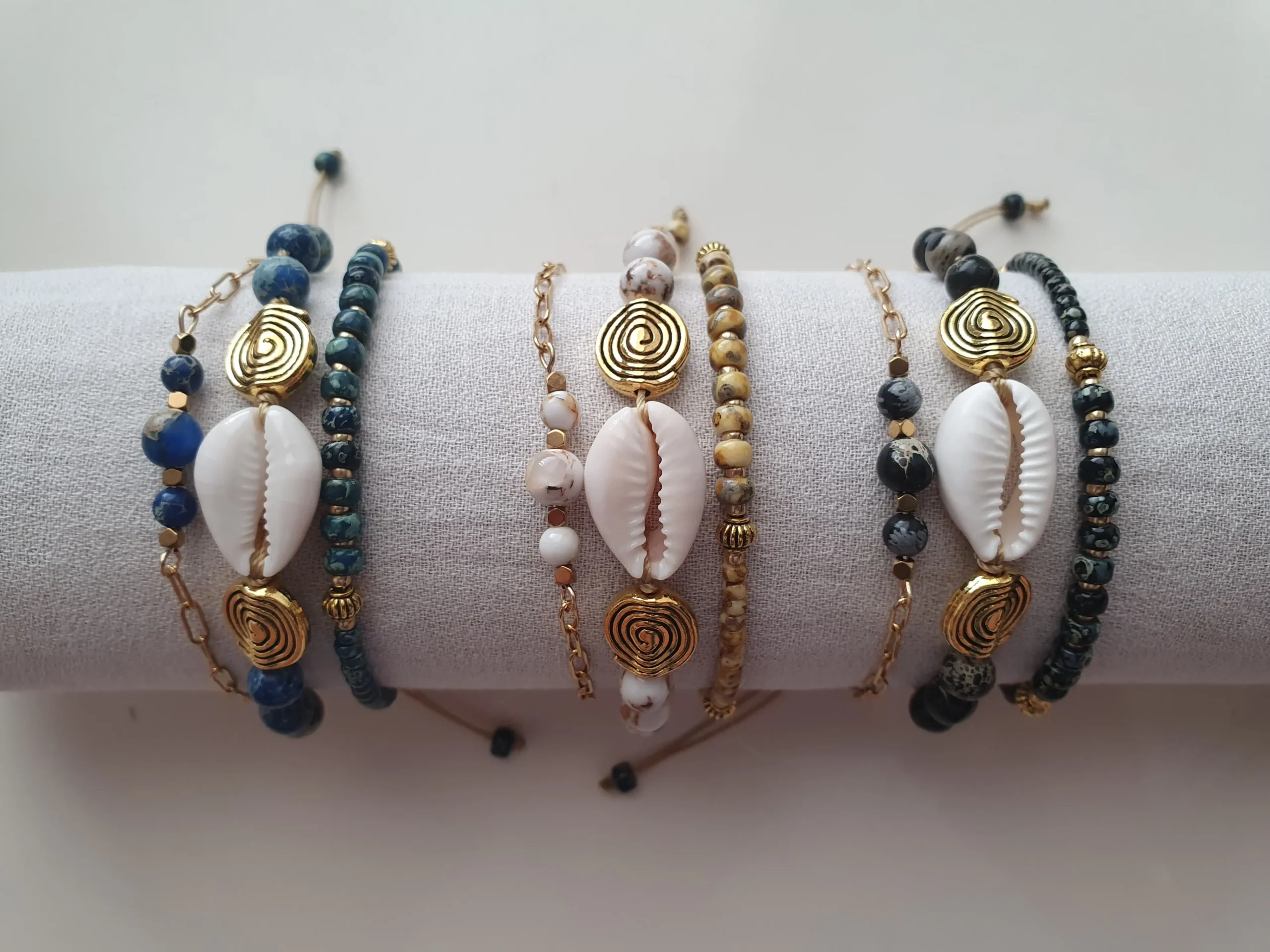 Bracelet Trio Ocealis avec coquillage cauri et perles de pierre naturelle. Ensemble. Vue sur coussin