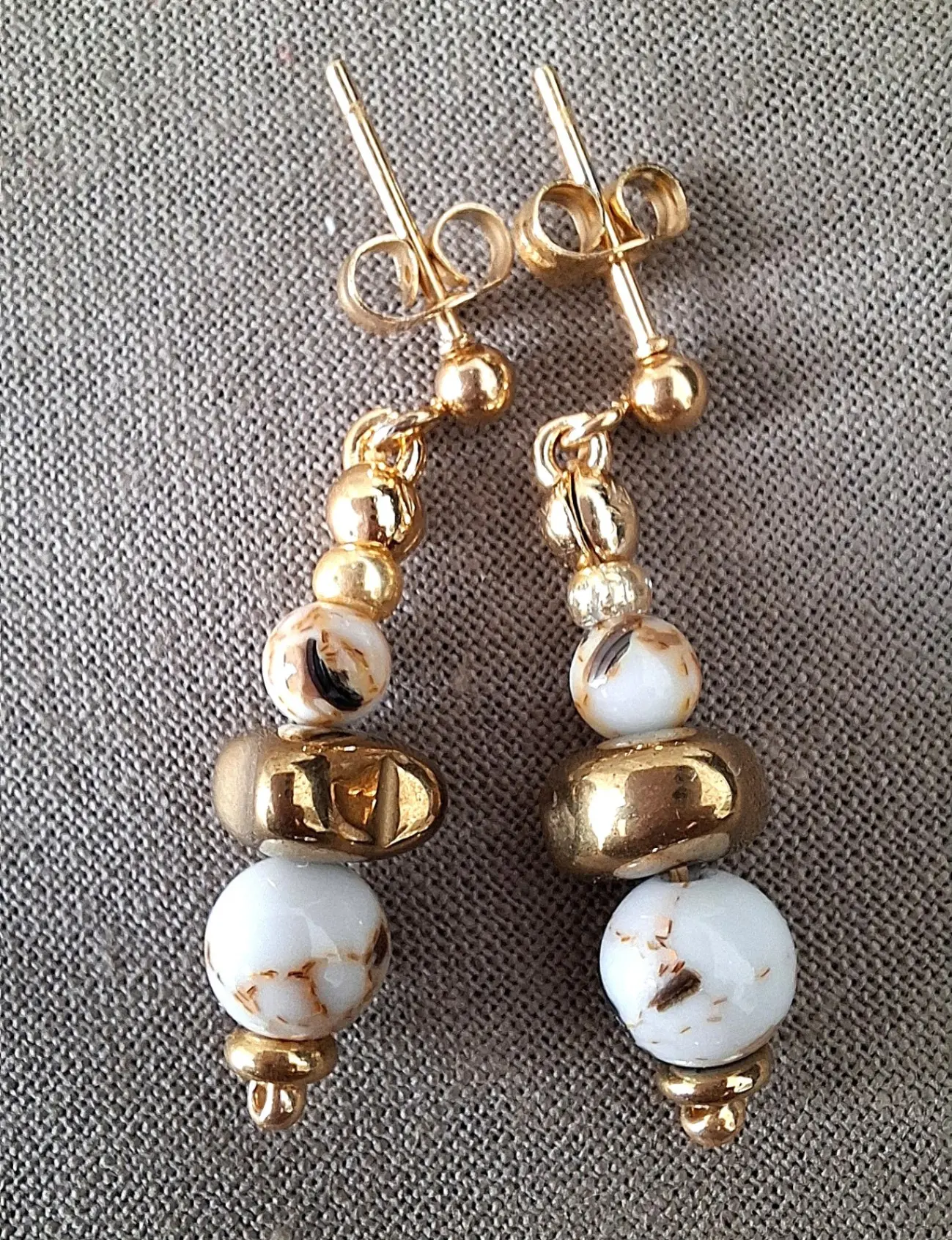 Boucles d'oreilles Marama en perles de nacre et hématite doré montées sur clou en acier inoxydable. Vue à plat.