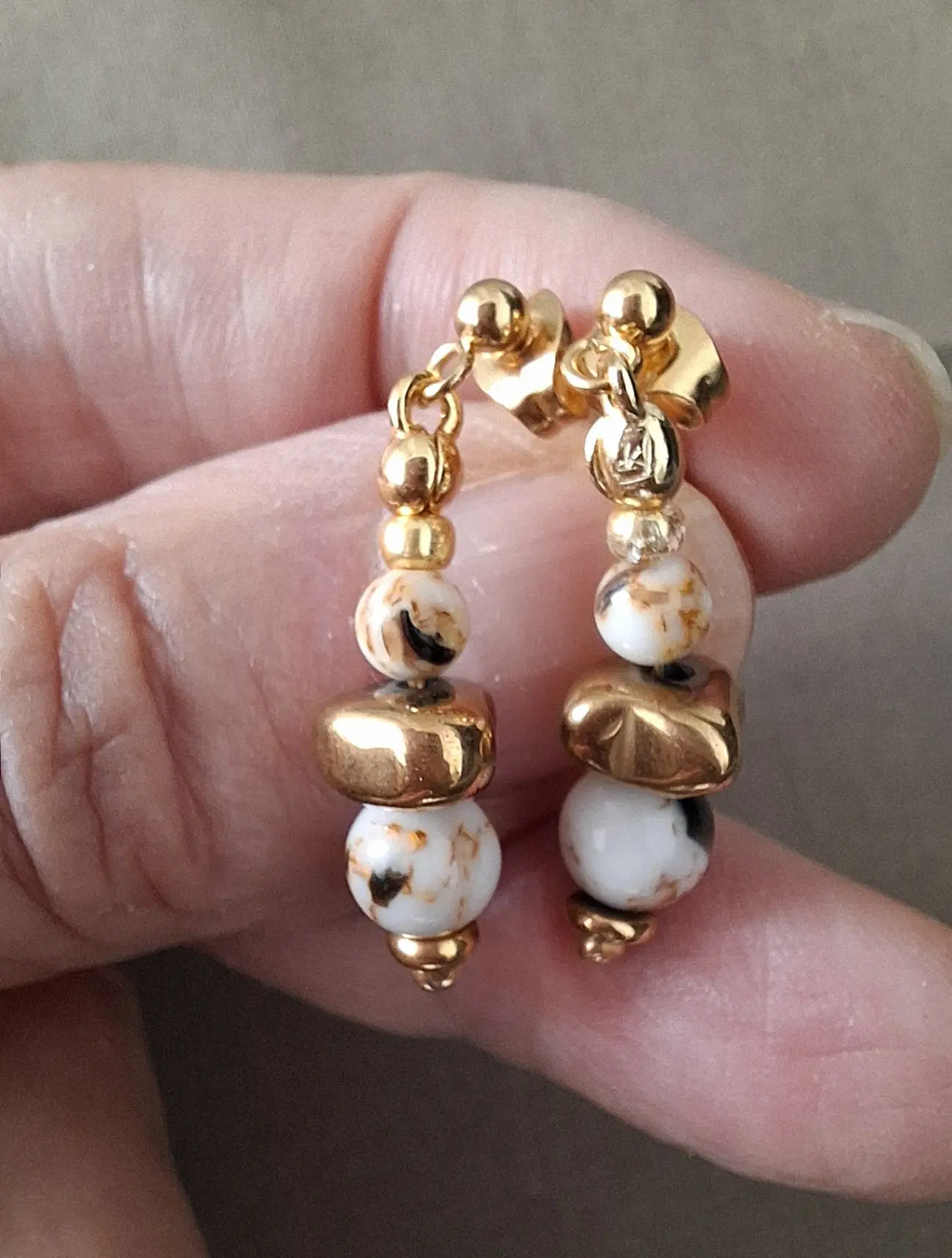 Boucles d'oreilles Marama en perles de nacre et hématite doré montées sur clou en acier inoxydable. Vue dans la main.