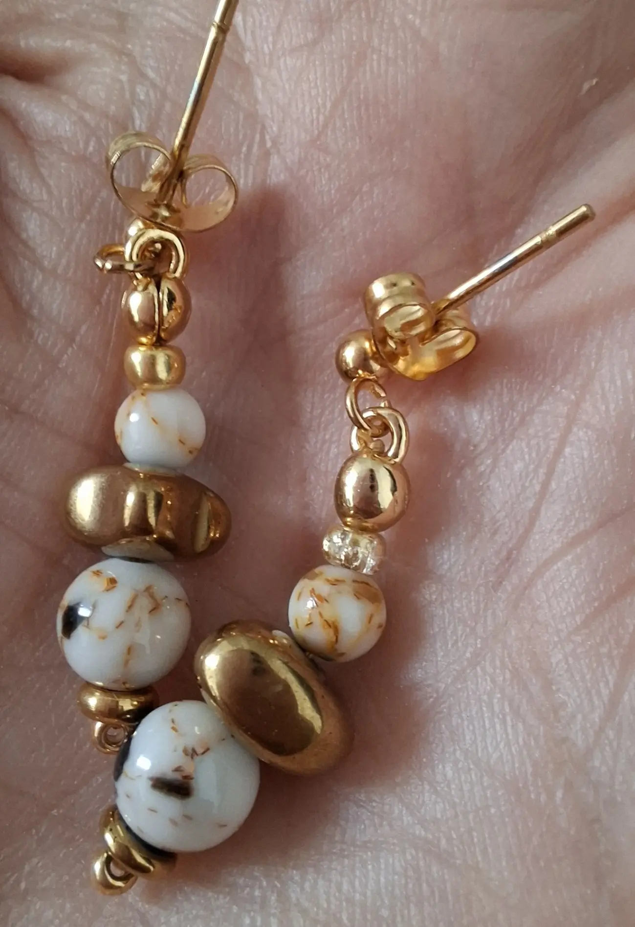 Boucles d'oreilles Marama en perles de nacre et hématite doré montées sur clou en acier inoxydable. Vue dans la main.