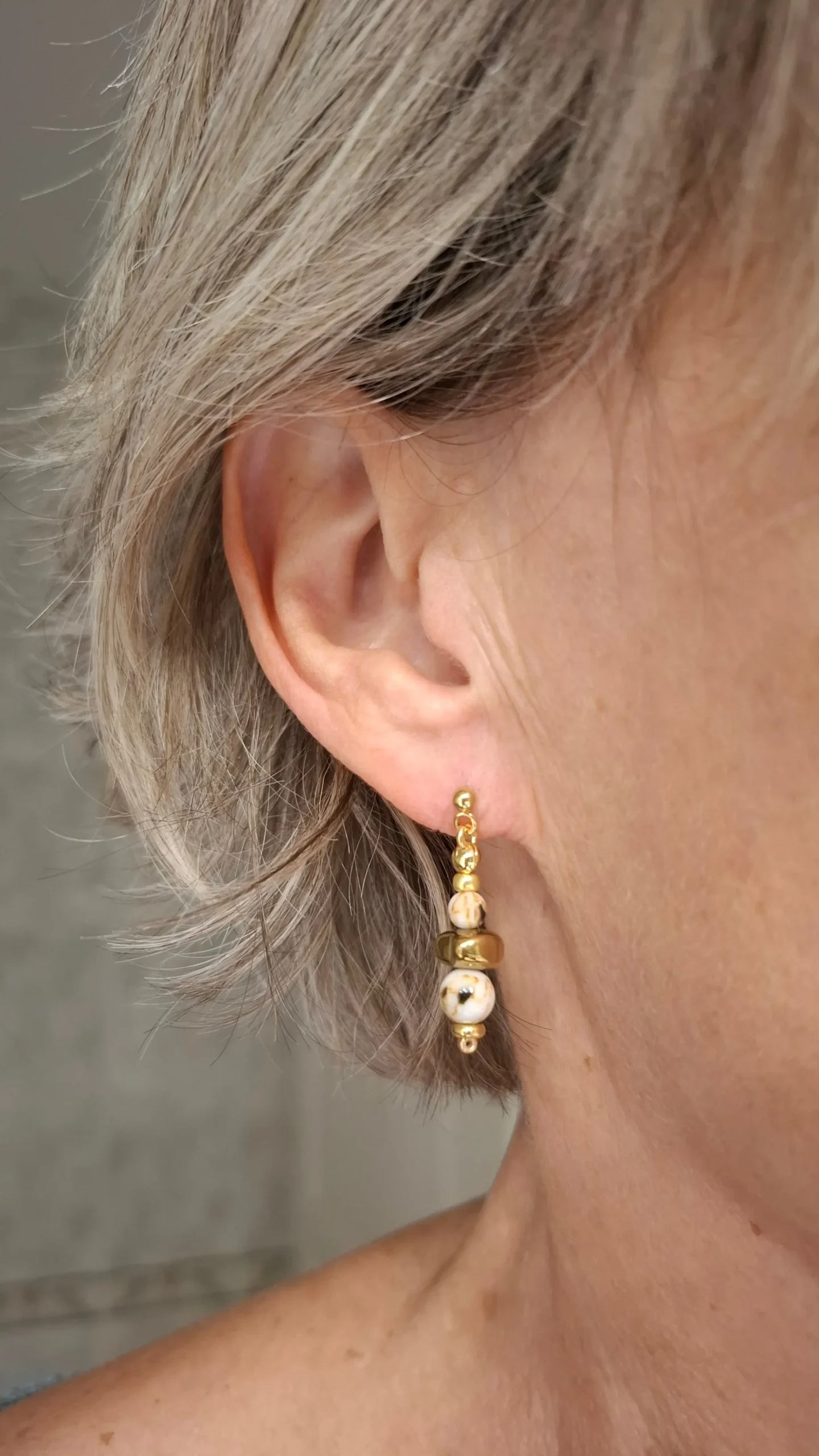 Boucles d'oreilles Marama en perles de nacre et hématite doré montées sur clou en acier inoxydable. Vue portées.