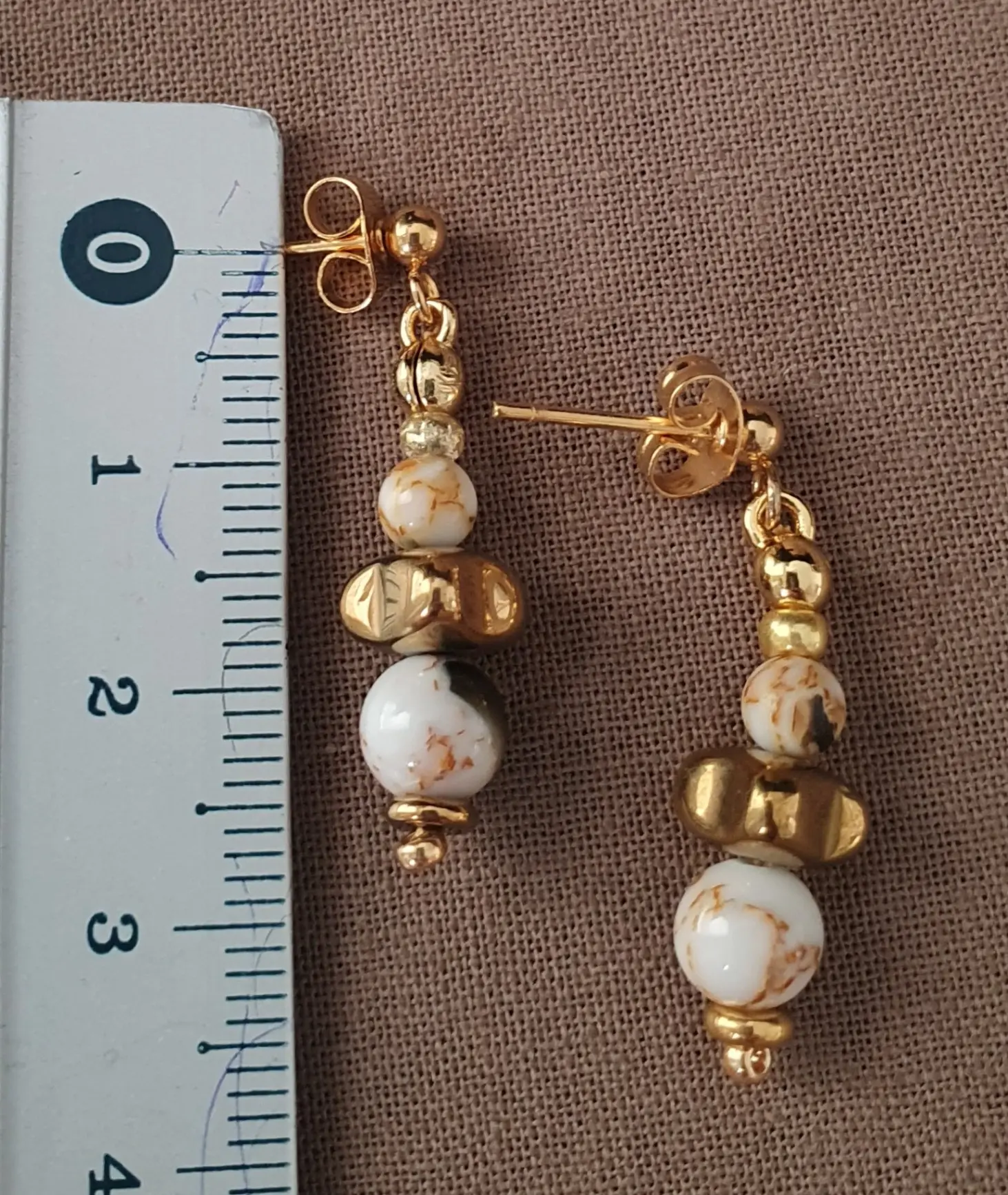 Boucles d'oreilles Marama en perles de nacre et hématite doré montées sur clou en acier inoxydable. Vue taille.