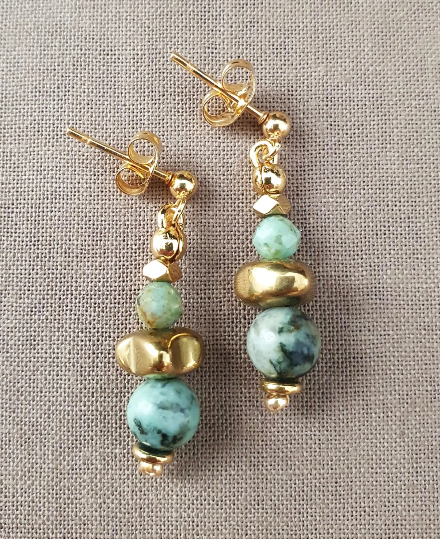 Boucles d'oreilles Marama en perles de turquoise africaine et hématite doré montées sur clou en acier inoxydable. Vue à plat.