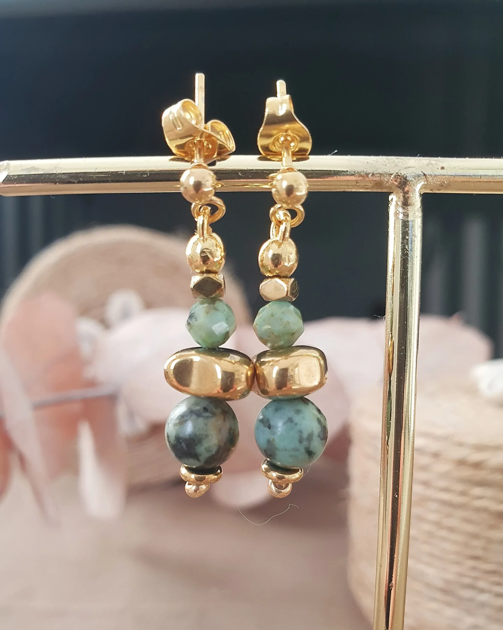 Boucles d'oreilles Marama en perles de turquoise africaine et hématite doré montées sur clou en acier inoxydable. Vue sur portant.