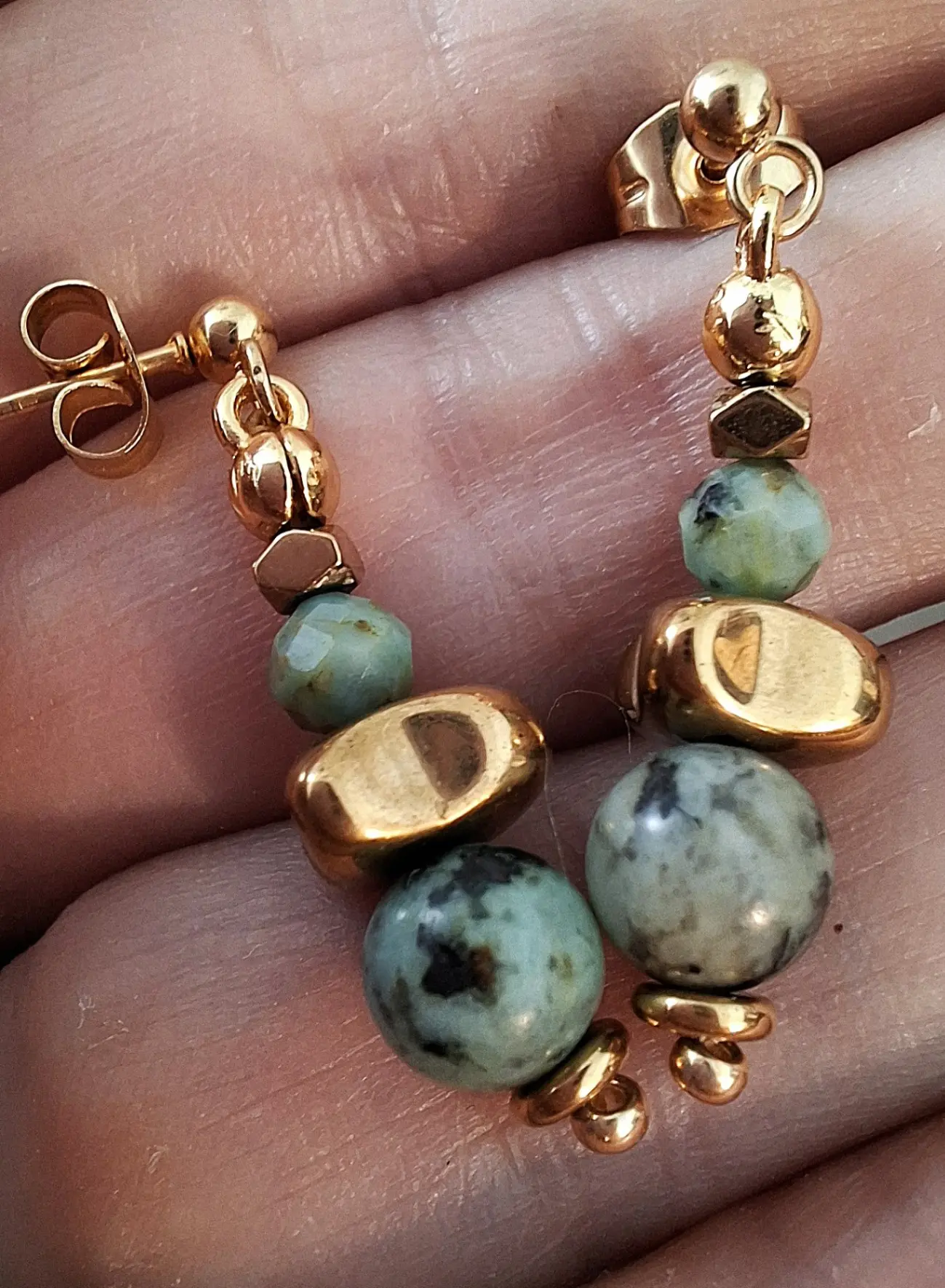 Boucles d'oreilles Marama en perles de turquoise africaine et hématite doré montées sur clou en acier inoxydable. Vue dans la main.